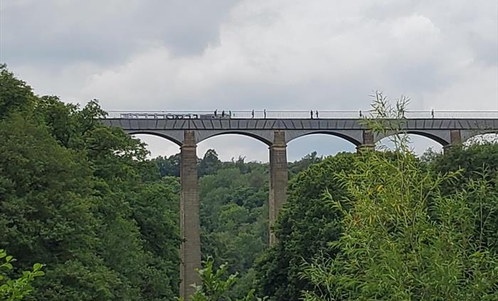 Looking at Pontcysylite Aqueduct from below, seeing the arches as people and a long boat cross